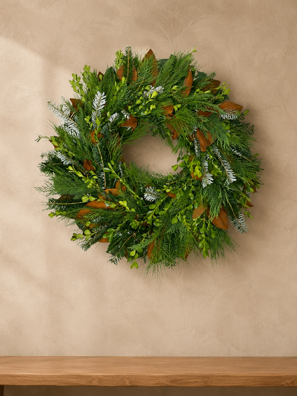 Classic Evergreen fresh wreath of boxwood, magnolia, Leyland cypress, pine, and Fraser fir on a plaster wall above a wood bench