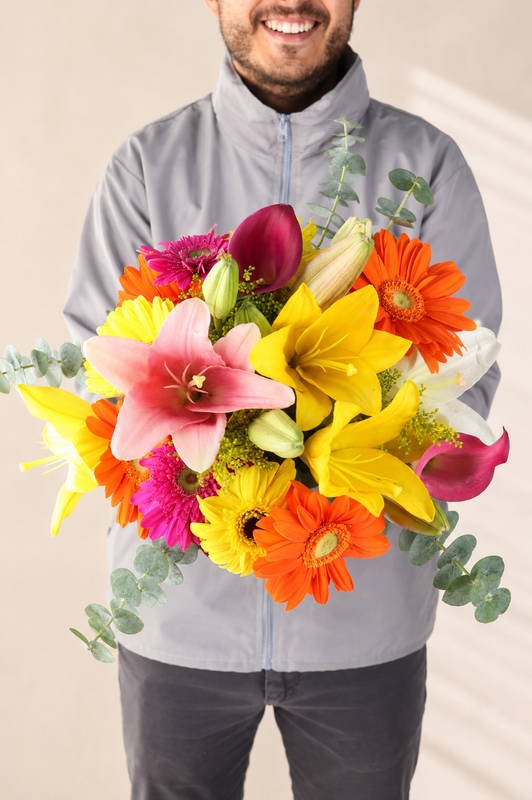 Man holding a bright bouquet of pink lilies, orange gerbera daisies and yellow lilies