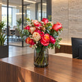 Bouquet of coral roses, ranunculus and eucalyptus in a glass vase on a wood reception desk