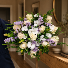 Load image into Gallery viewer, White and cream flowers with lavender accents in a hand-held bouquet in an entryway

