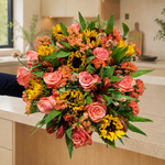 Coral roses and sunflowers with orange accents in a bouquet on a kitchen counter