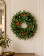 Holiday Cheer Wreath, a fresh cypress and boxwood wreath with magnolia leaves, hanging on a paneled wall beside a gold mirror