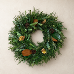 Home for the Holidays fresh holiday wreath of cedar, fir, eucalyptus, magnolia, dried orange, cinnamon sticks, and pinecones on a plaster wall