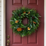 Home for the Holidays wreath on a deep red front door, with cedar, eucalyptus, magnolia, dried orange, cinnamon sticks, and pinecones