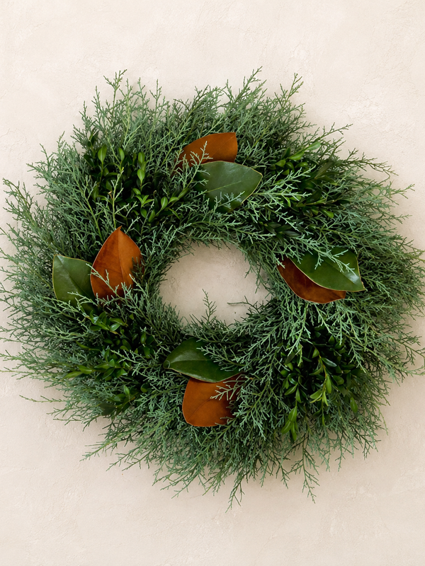 Holiday Cheer Wreath, a fresh 18-inch wreath of Carolina Sapphire cypress, boxwood, and magnolia leaves, on a plaster wall
