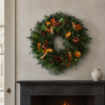 Spice Up the Holidays wreath above a black marble fireplace, with fir, boxwood, magnolia, dried orange slices, cinnamon-stick bundles, and pinecones