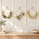 The Gilded Wings Trio, three gold wing-style wreaths, styled on a cream paneled wall