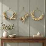 The Gilded Wings Trio, three gold wing-style wreaths, styled on a sage green paneled wall