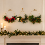 The Golden Hoops Trio, three gold ring wreaths with greenery and red, cream, and gold accents, hung above a garland-draped fireplace mantel