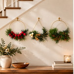 The Golden Hoops Trio, three gold ring wreaths with greenery and red, cream, and gold accents, hung on a staircase wall above a wood console