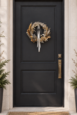 The Starlight Wreath hanging on a black front door with a white ribbon