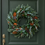 The Welcome Wreath hanging on a dark green front door